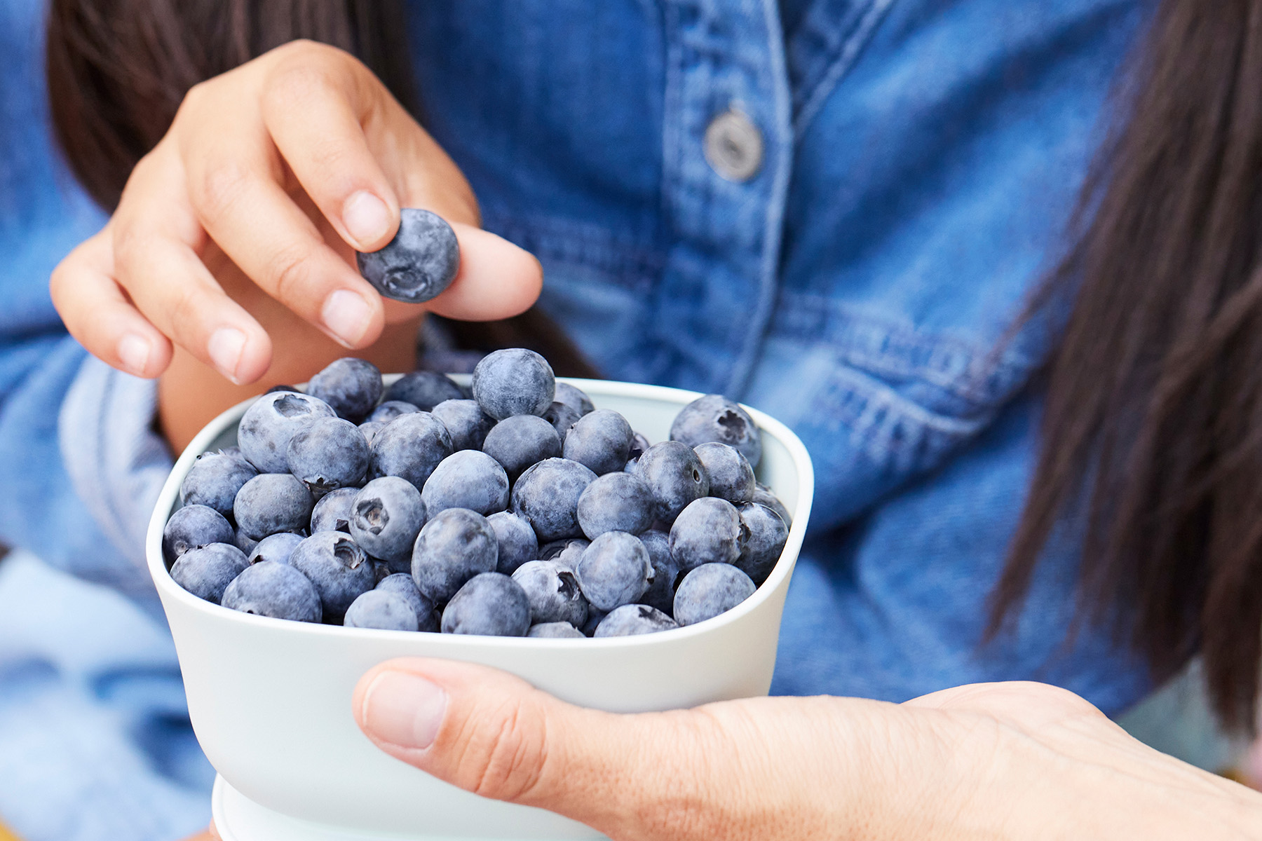 A child digging their hand into a beautiful bowl of blueberries.