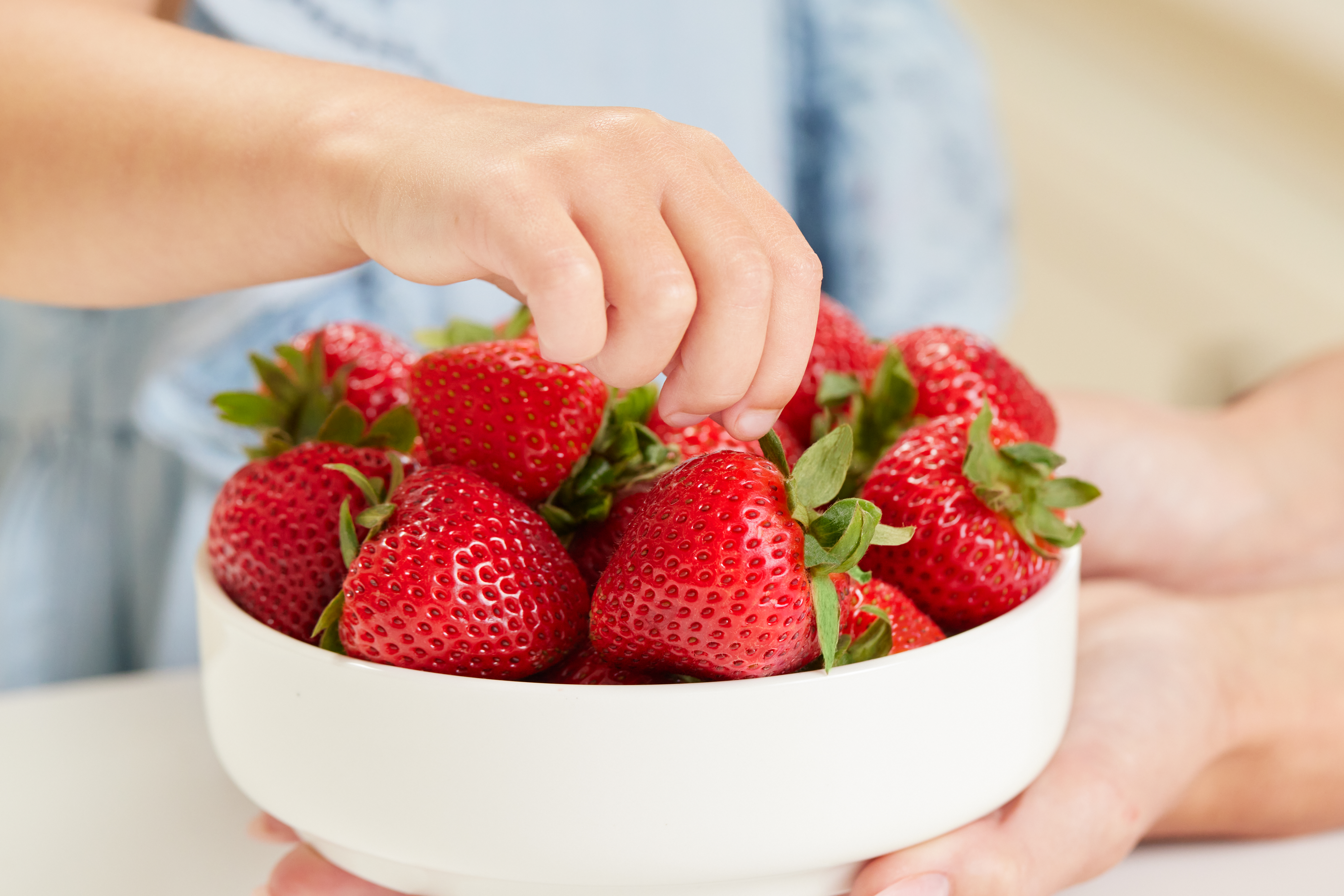 A child digging their hand into a beautiful bowl of strawberries.