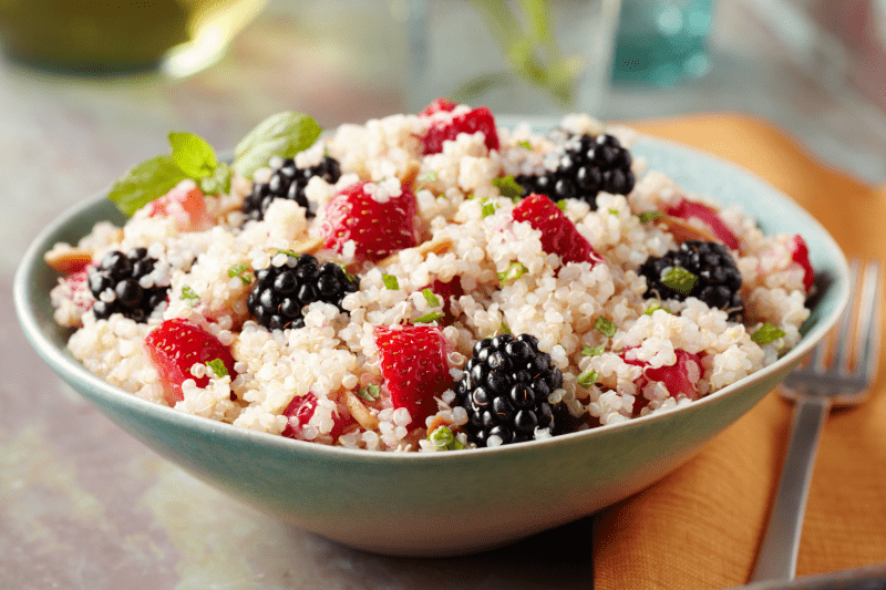 Fluffy quinoa mixed with juicy strawberries and blackberries sit in a blue-gray bowl.