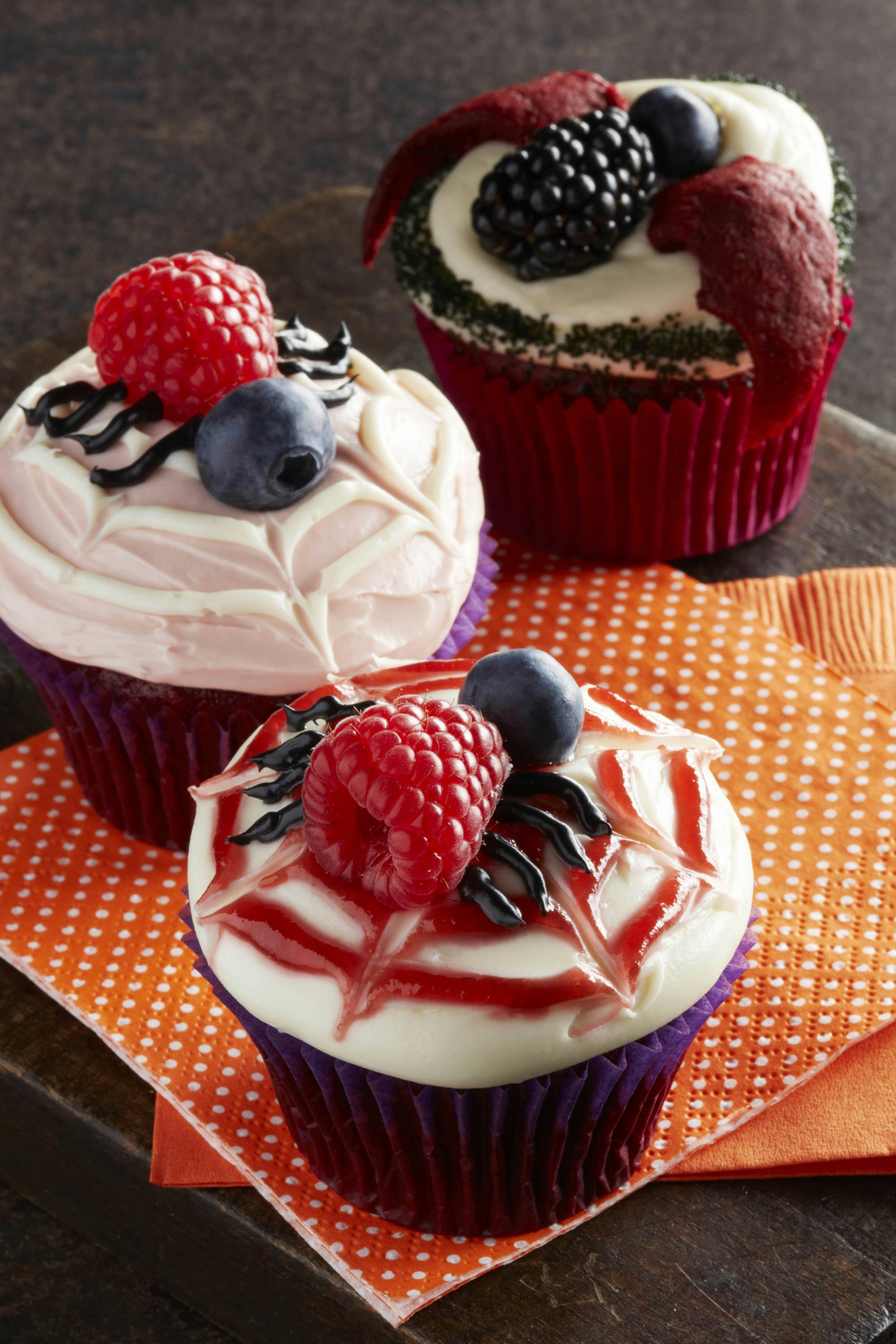 Three berry cupcakes decorated with a halloween theme and topped with berries