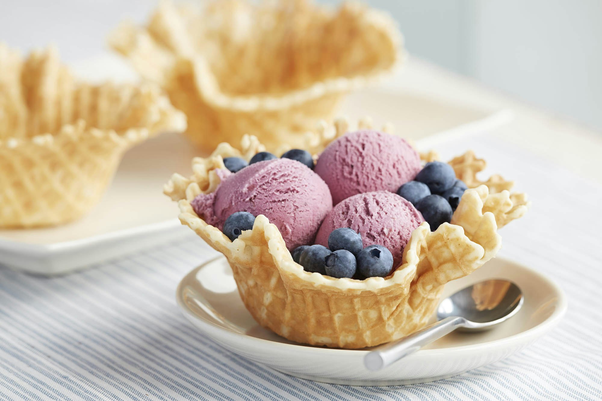 A waffle cone with scoops of blueberry ice cream and blueberries