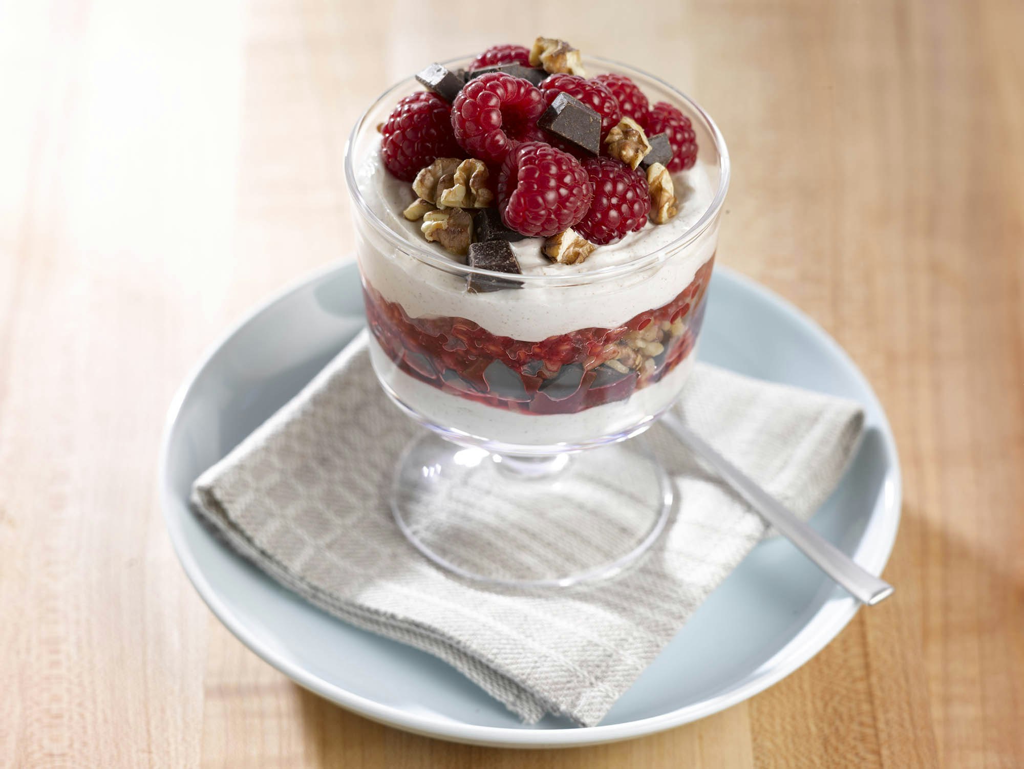 Glass of yogurt parfait layered with raspberries and dark chocolate granola 